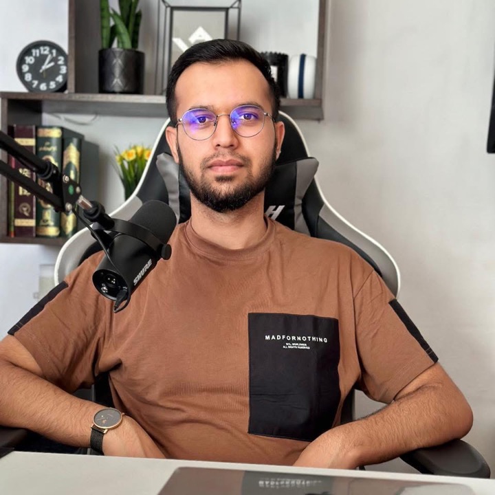 Wasim Jalali at his desk, in a brown t-shirt, with a microphone and a bookshelf behind him